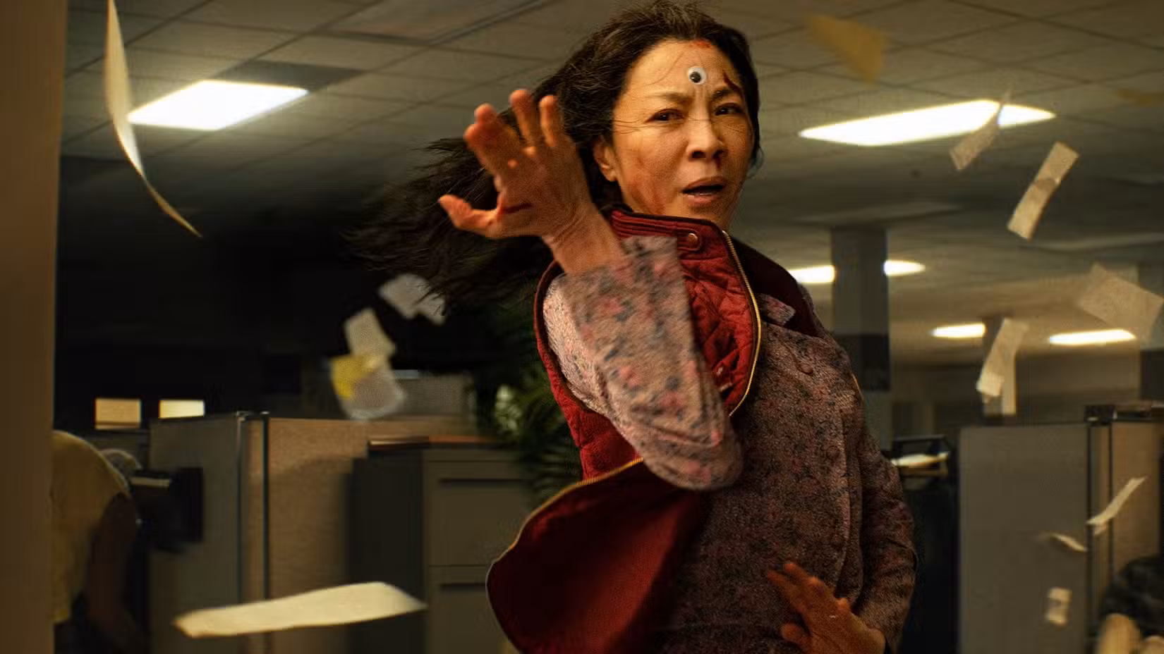 Uma Michelle Yeoh ensanguentada e com um olho arregalado colado na testa faz uma pose de artes marciais em Everything Everywhere All at Once
