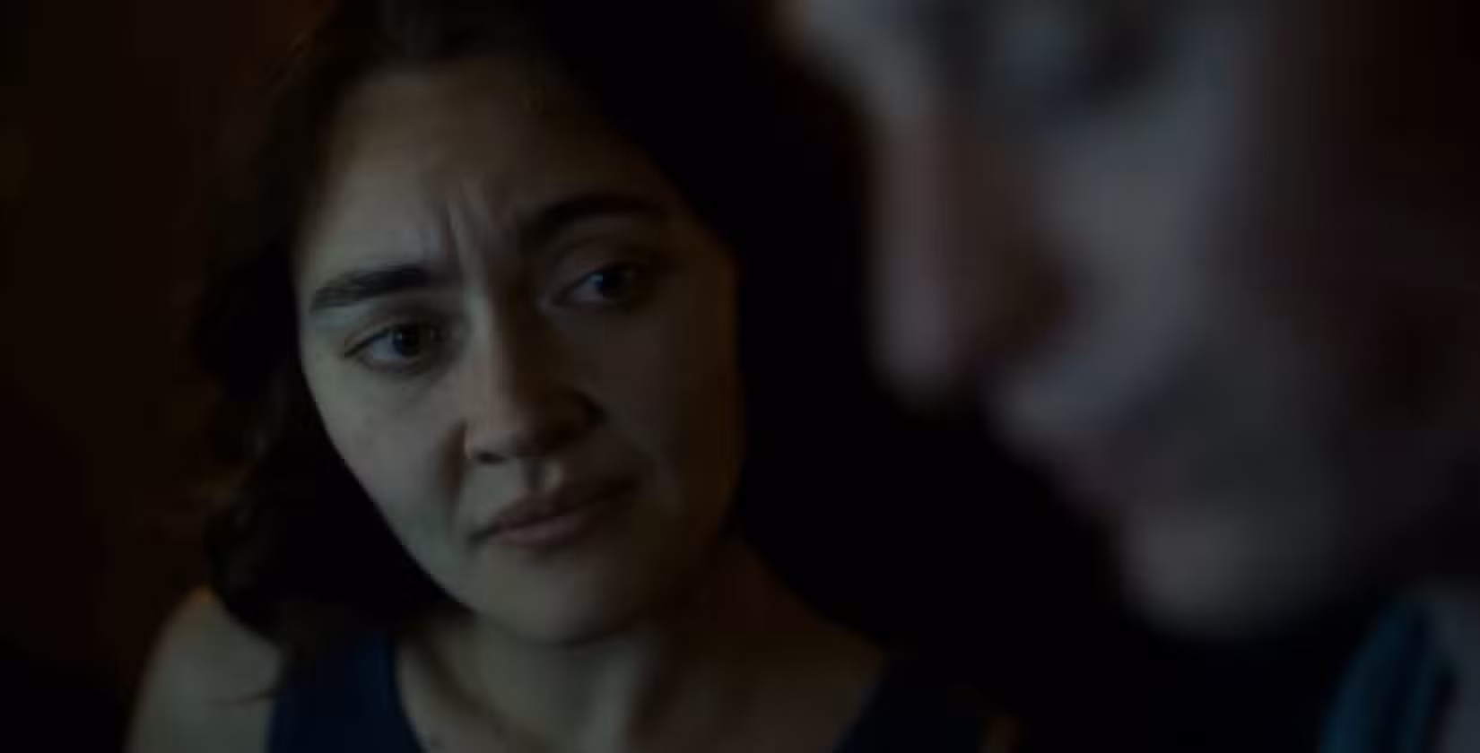 O ator Jamie Taylor Ballesta, uma mulher morena de cabelos castanhos curtos, olha preocupado para seu parceiro de cena