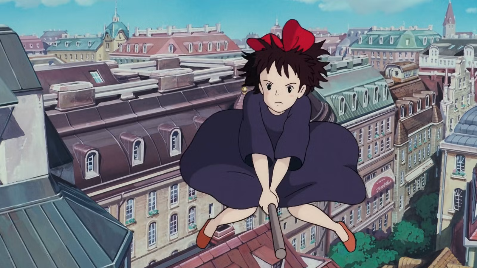 Kiki, uma garota de anime com cabelo preto e um laço vermelho no topo, monta uma vassoura sobre uma paisagem urbana de estilo europeu no Kiki's Delivery Service do Studio Ghibli.