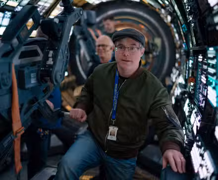 O autor do Projeto Hail Mary, Andy Weir, no set do filme, cercado por um túnel de painéis e dispositivos iluminados