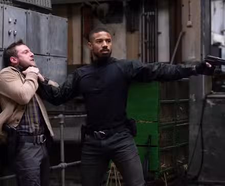 Michael B. Jordan como Navy SEAL John Clark prende um homem na parede pela garganta com uma das mãos e aponta uma arma com a outra em Without Remorse