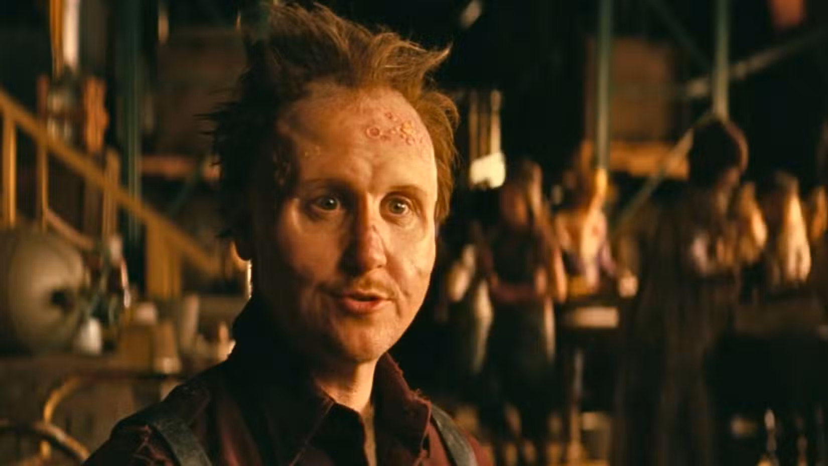 Uma imagem de Thaddeus da 2ª temporada de Fallout. Ele tem cabelo curto espetado e um rosto que parece marcado por cicatrizes e varíolas. 