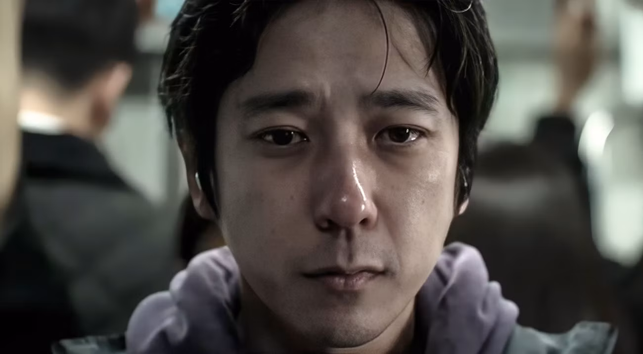The Lost Man (Kazunari Ninomiya), um jovem japonês de moletom, visto em close com nariz vermelho e olhos lacrimejantes como se estivesse chorando, na Saída 8