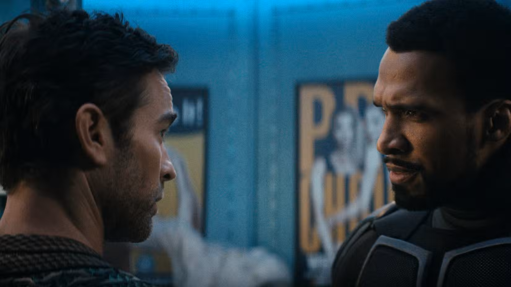 Black Noir (Nathan Mitchell) parece chateado com The Deep (Chace Crawford) enquanto eles estão em uma sala cheia de pôsteres.