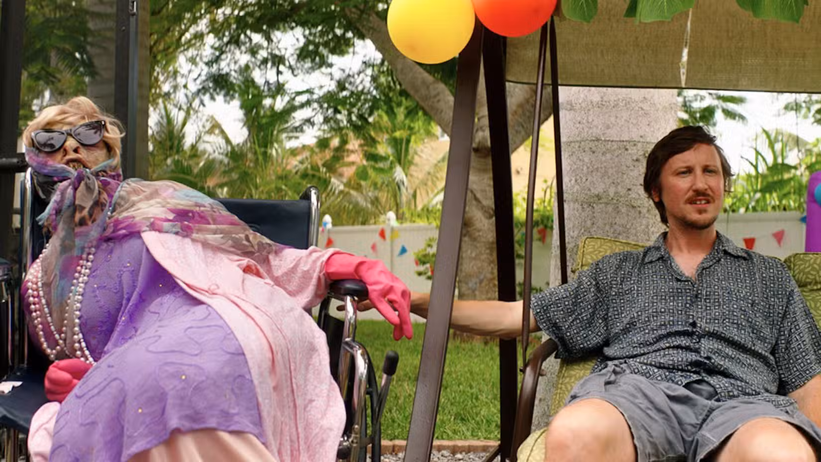 Uma imagem de Johnny Pemberton no filme de comédia de ação Sereia. Mostra Doug (Johnny) sentado, com a mão no braço de uma cadeira de rodas. Uma sereia, vestida com roupas antigas, óculos escuros e uma peruca ruim, senta ao lado dele.