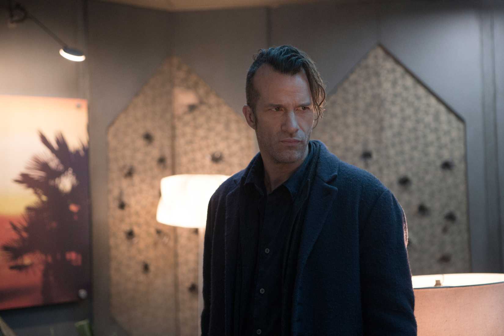 Joe Miller (Thomas Jane), um homem estreito e carrancudo, todo vestido de preto e com um lado da cabeça raspado, em The Expanse