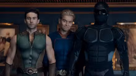 Homelander (Antony Starr) está atrás de The Deep (Chace Crawford) e Black Noir (Nathan Mitchell) na Vought Tower enquanto Deep parece muito nervoso.