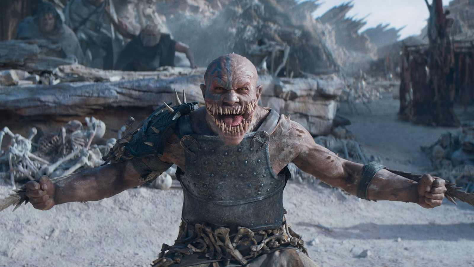 Baraka (CJ Bloomfield), um homem blindado com muitos dentes, fica na frente de uma vila e crânios montados em pontas em Mortal Kombat 2.